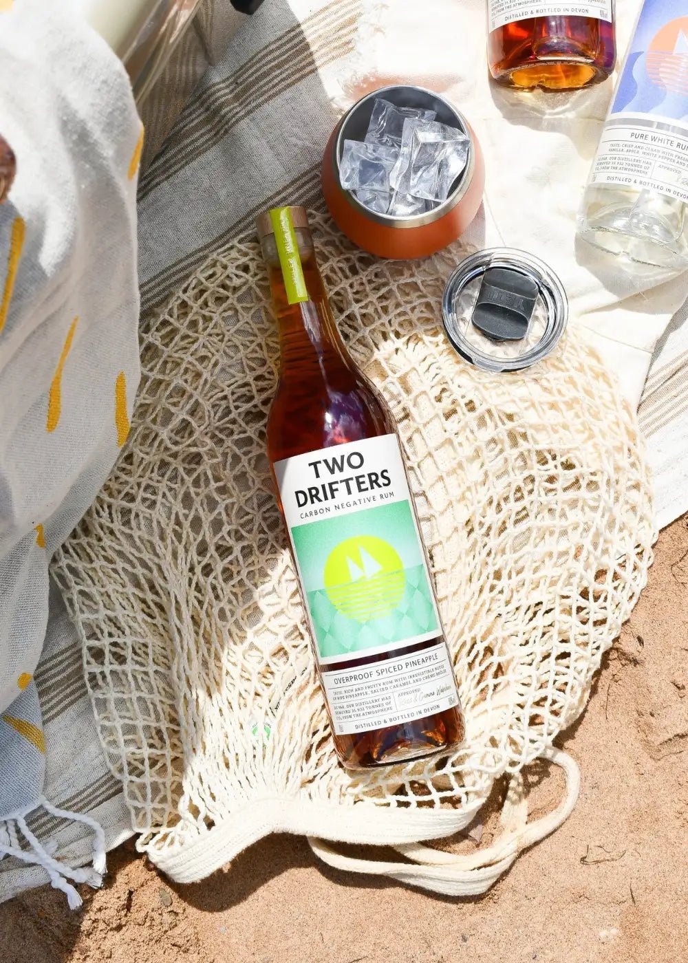 Bottle of Two Drifters Overproof Pineapple rum on a net bag on a beach