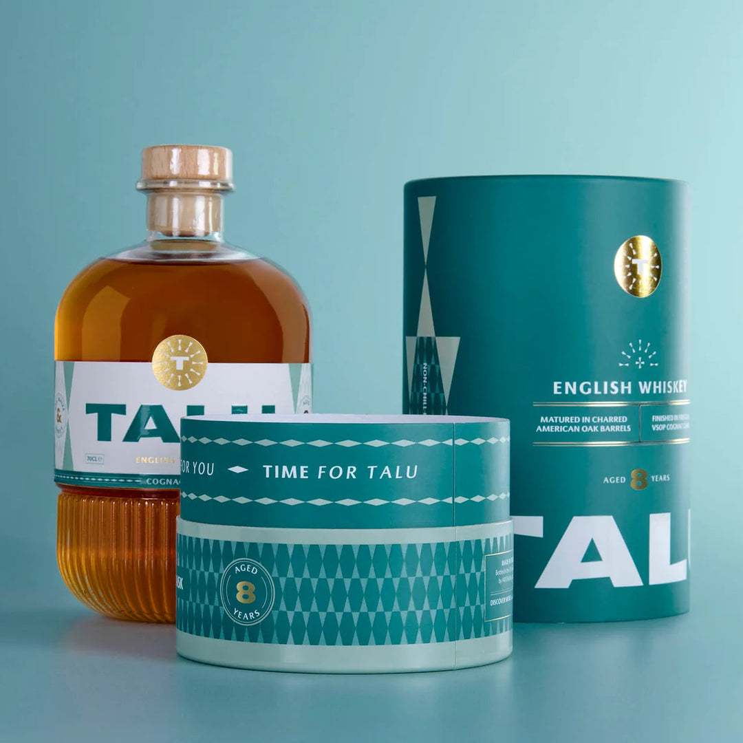 A bottle of Talu English Whiskey alongside its teal cylindrical packaging and a matching teal tin, set against a solid light blue background.