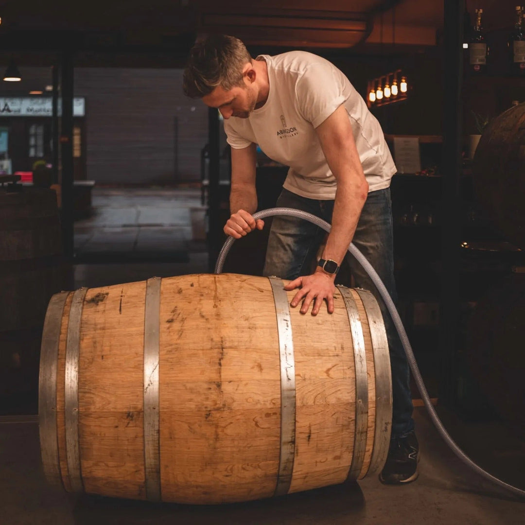 Distiller Jordan filling a wooden barrel in a dimly lit room