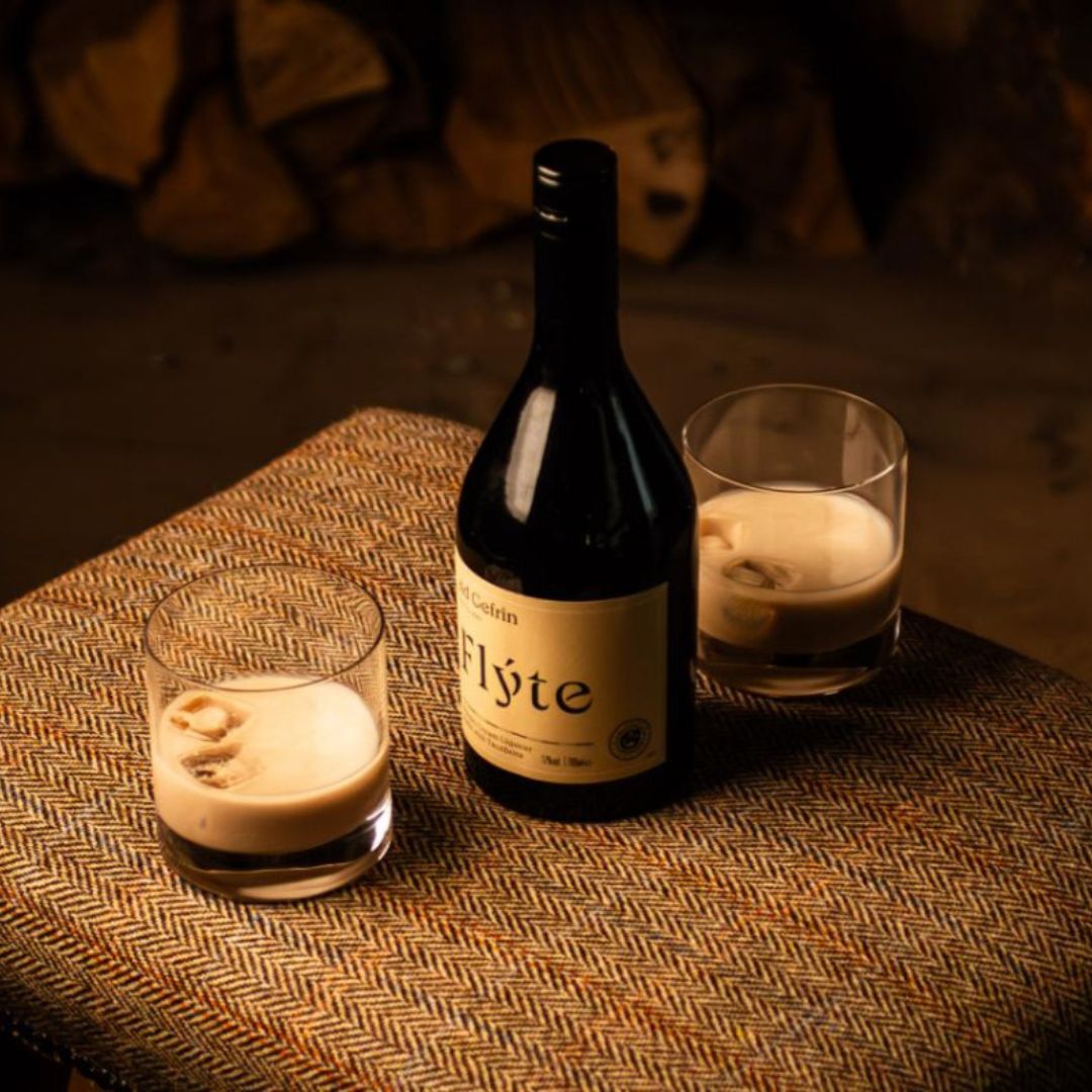 Bottle of Flyte Cream Liqueur with two glasses on a textured tweed covered surface, warm lighting.