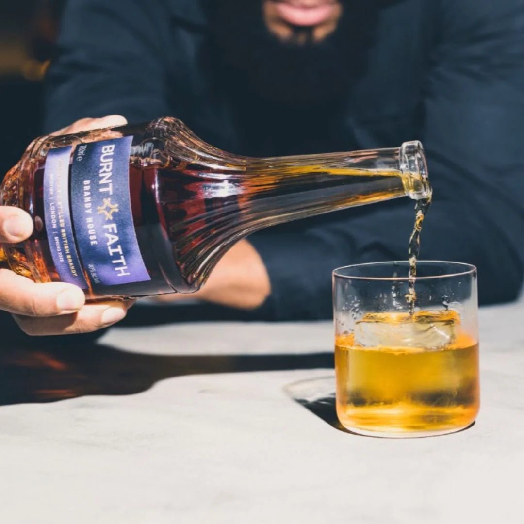 Person pouring Burnt Faith brandy into a glass on a light surface.