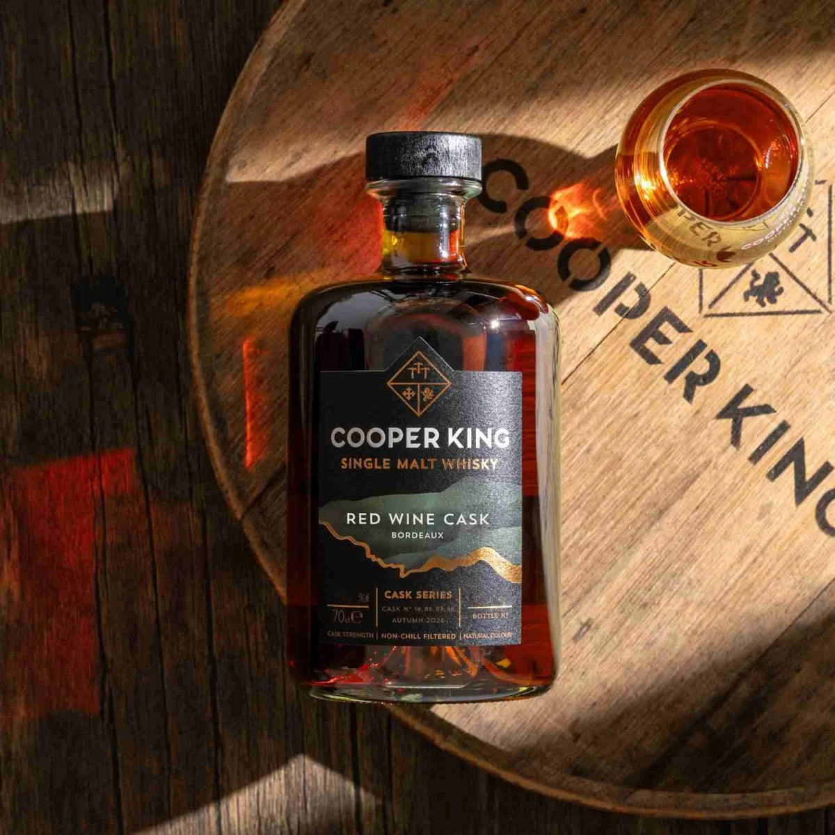 Cooper King Red Wine Cask whisky on an oak cask head beside a filled whisky glass