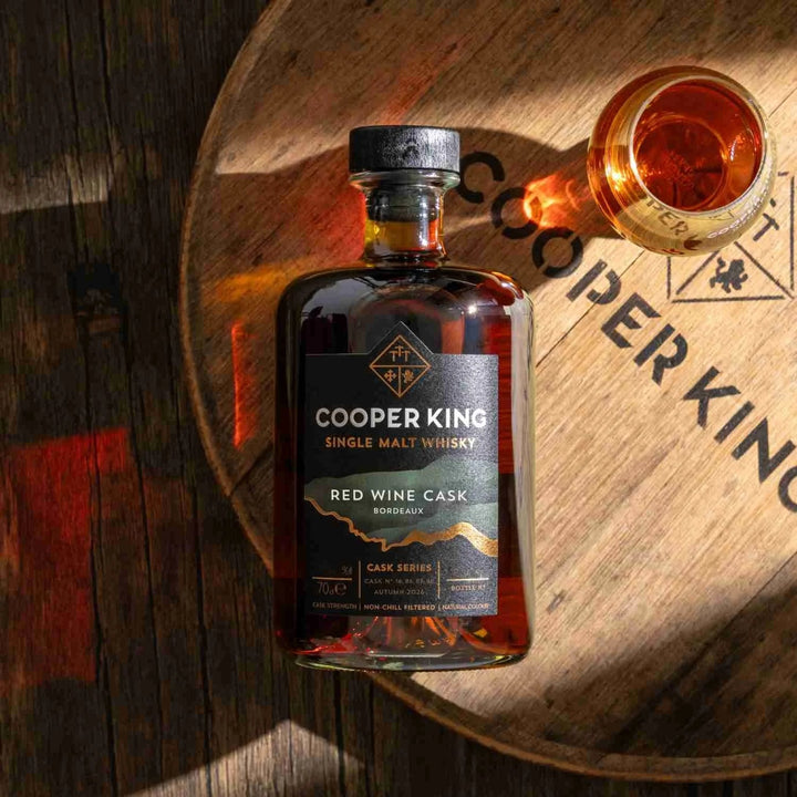 Cooper King Red Wine Cask whisky on an oak cask head beside a filled whisky glass