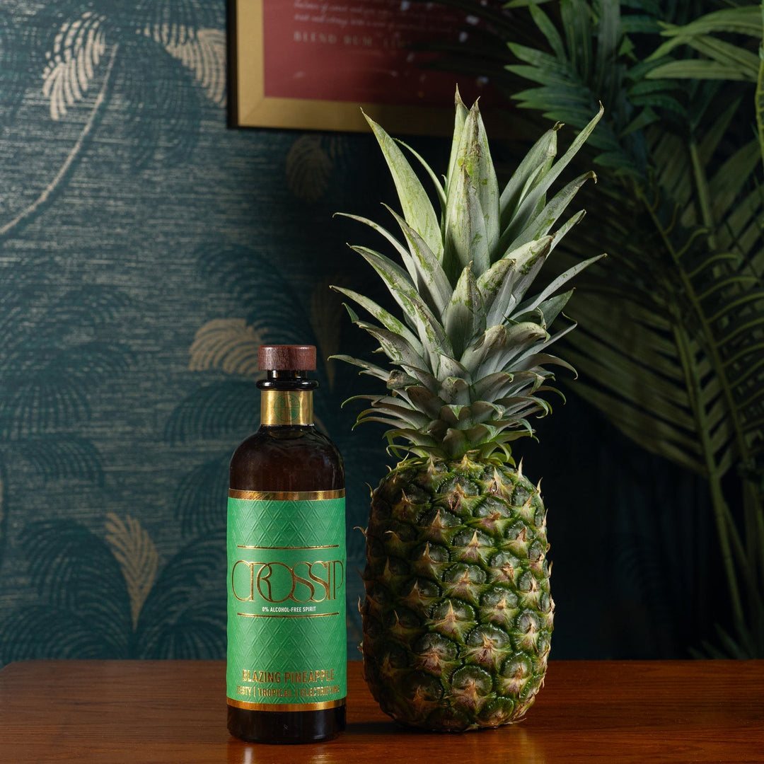 Bottle of Crossip Blazing Pineapple with a pineapple on a wooden table against a decorative wall.