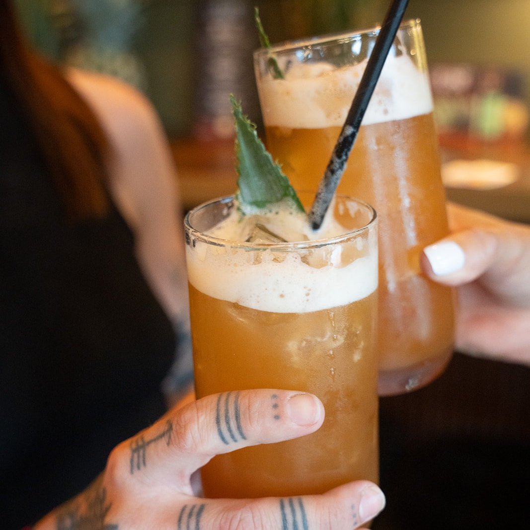 Two hands holding glasses of iced drinks with a blurred background