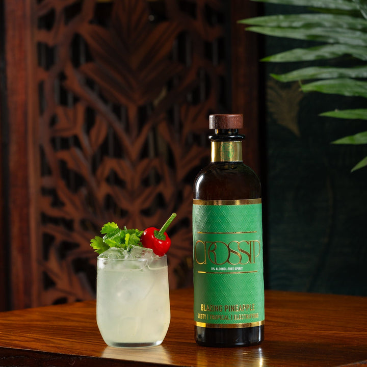 Bottle of Crossip Blazing Pineapple on a wooden table with a cocktail garnished with a pepper and coriander leaf.