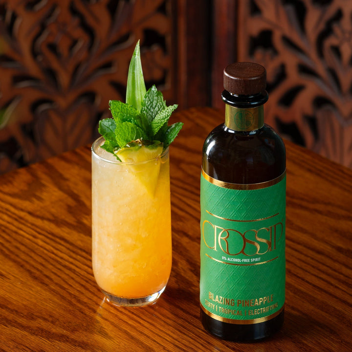 Bottle of Crossip Blazing Pineapple with a cocktail garnished with mint on a wooden surface.