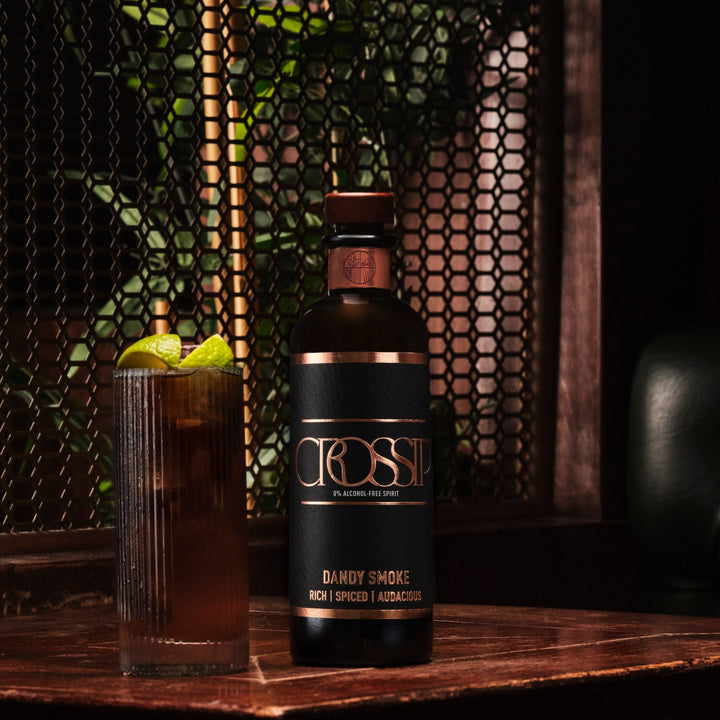 Bottle of Crossip Dandy Smoke with cola garnished with lime on a wooden surface.