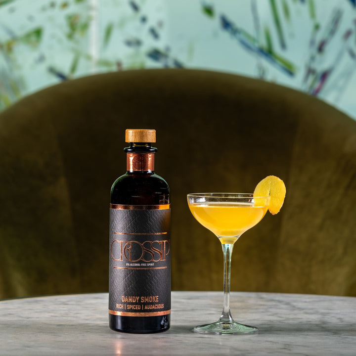 Bottle of Crossip Dandy Smoke and a cocktail with a lemon wedge on a table.