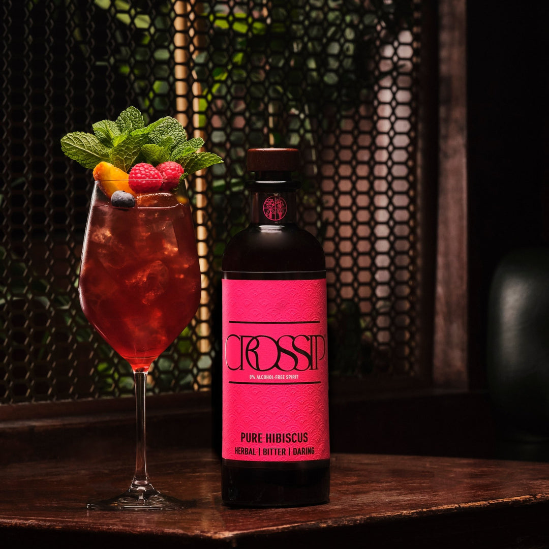 Bottle of Crossip Pure Hibiscus with a cocktail garnished with berries and mint leaves on a wooden surface.