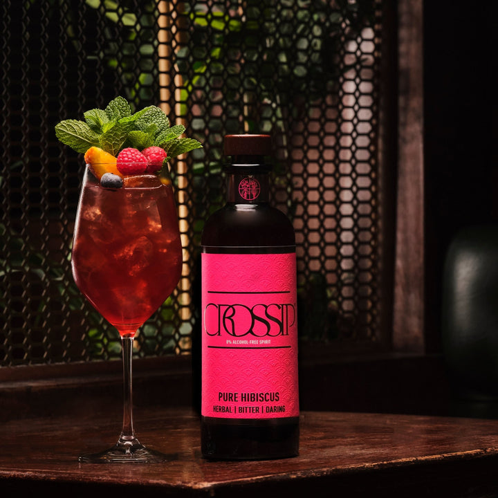 Bottle of Crossip Pure Hibiscus with a cocktail garnished with berries and mint leaves on a wooden surface.