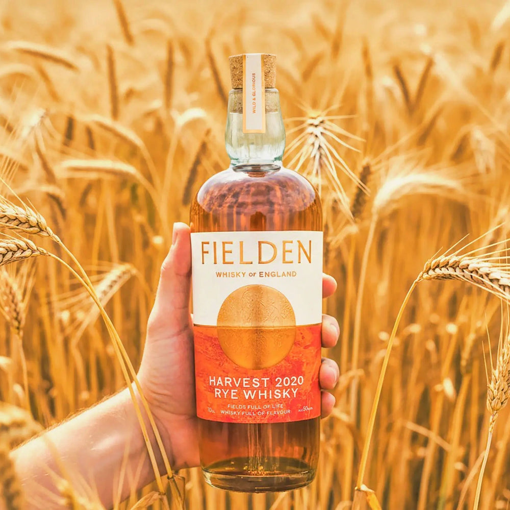 Hand holding a Fielden 2020 Harvest Rye Whisky bottle in a wheat field