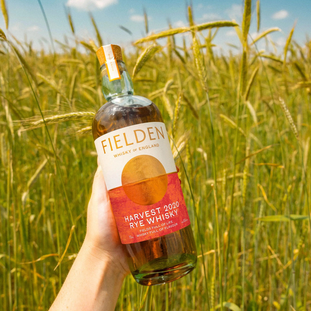 Bottle of Fielden Harvest 2020 Rye Whisky held in a field with a blue sky.