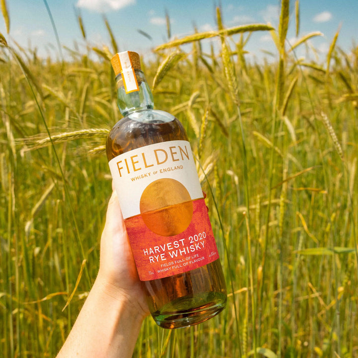 Bottle of Fielden Harvest 2020 Rye Whisky held in a field with a blue sky.