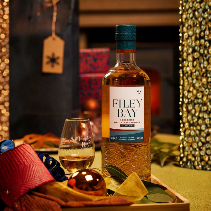 Filey Bay Yorkshire Single Malt Whisky bottle with a glass on a decorative tray in a festive setting.