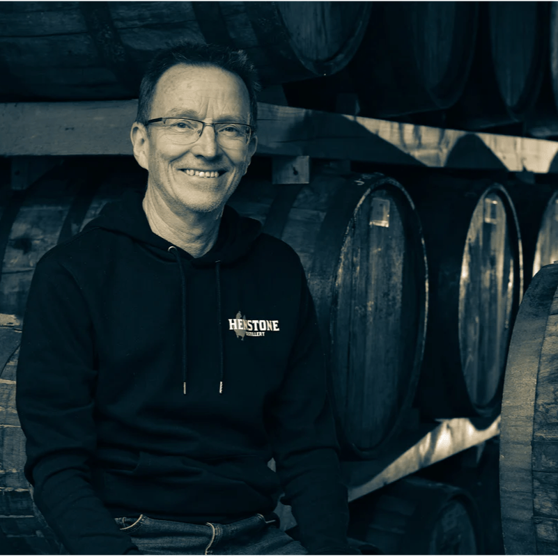 Chris Toller, co-founder of Henstone Distillery, Oswestry, wearing a black hoodie with 'Henstone' logo in front of wooden barrels