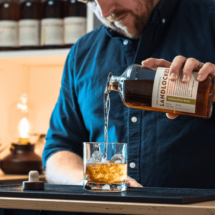 Man pouring Landlocked Pineapple Rum into a glass with ice cubes.
