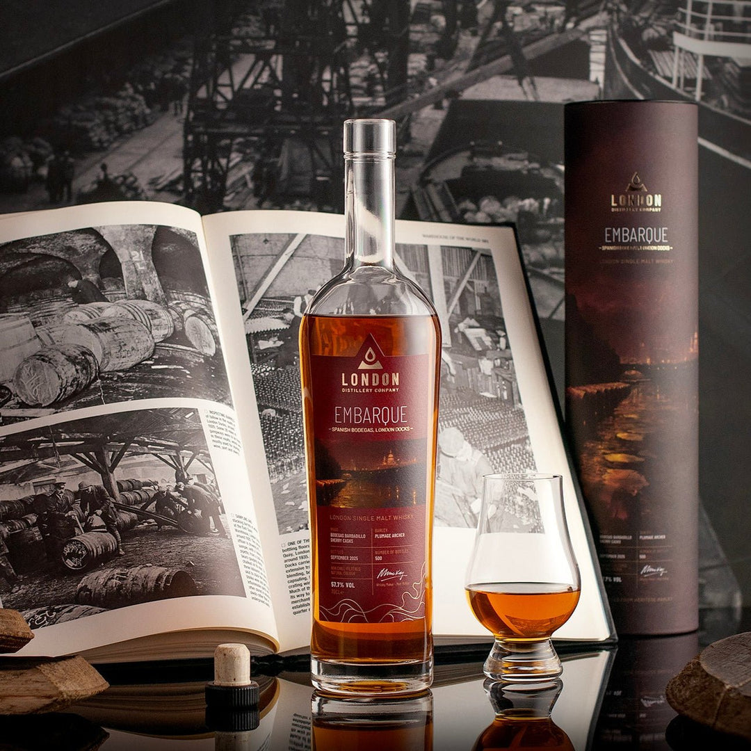 London Distillery Company Embarque whisky bottle with a glass and book in a dark setting