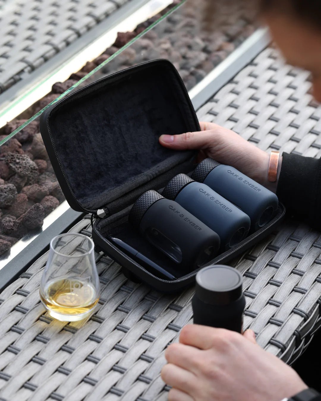Set of travel flasks in a carrying case on a table with a glass of liquid.