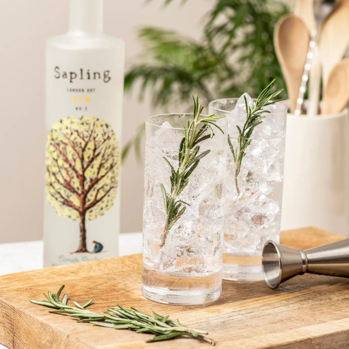 Sapling gin bottle with two cocktails in a glass on a wooden board.