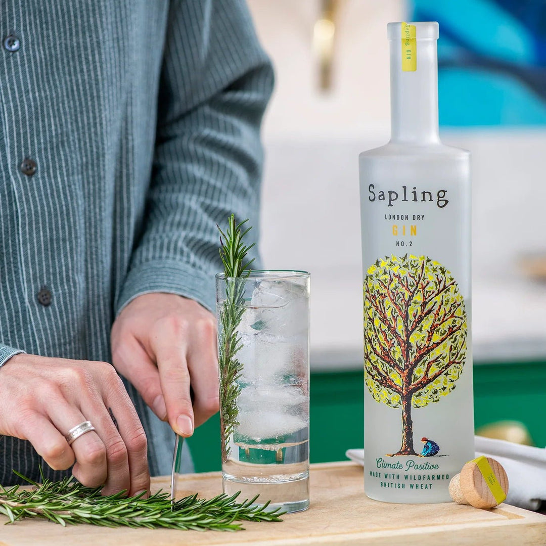 Person preparing a drink with a bottle of Sapling gin in the background