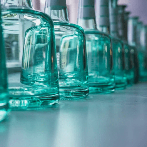 Row of teal glass bottles on a reflective surface