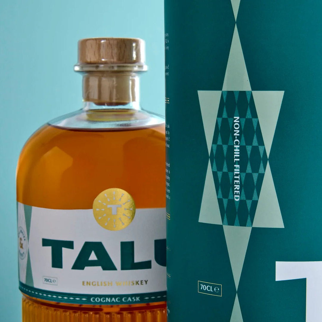 A bottle of TALU English Whiskey Cognac Cask whiskey with amber liquid, a wooden stopper, and a white label, shown next to its teal packaging box with geometric patterns.