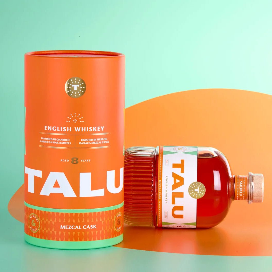 A bottle of Talu English Whiskey Mezcal Cask next to its orange cylindrical packaging container, set against a split mint green and orange background.