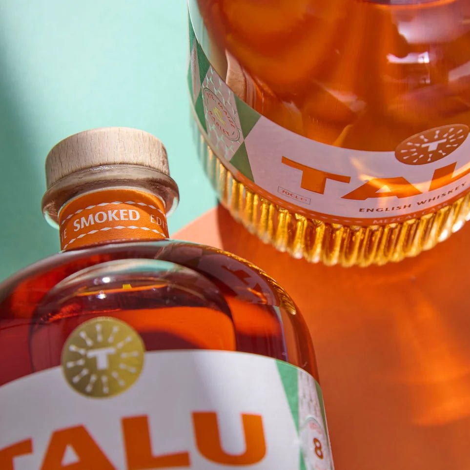 Two bottles of Talu Mezcal Cask Whiskey shown in a close-up, angled composition against a split teal and orange background.