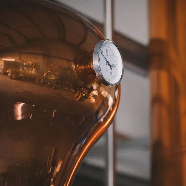 Close-up of a copper still with a thermometer used in distillation.