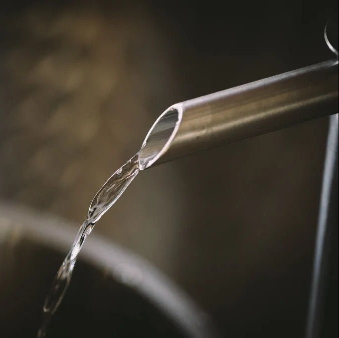 Spirit pouring from a metallic still spout into a container with a blurred background