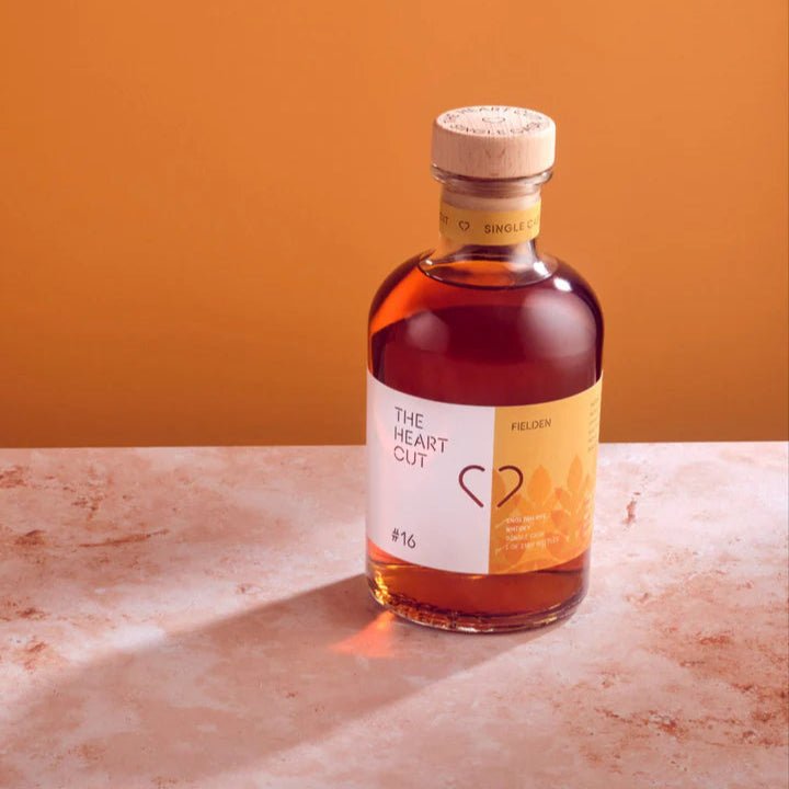 Bottle of 'The Heart Cut' whiskey on a marble surface with an orange background