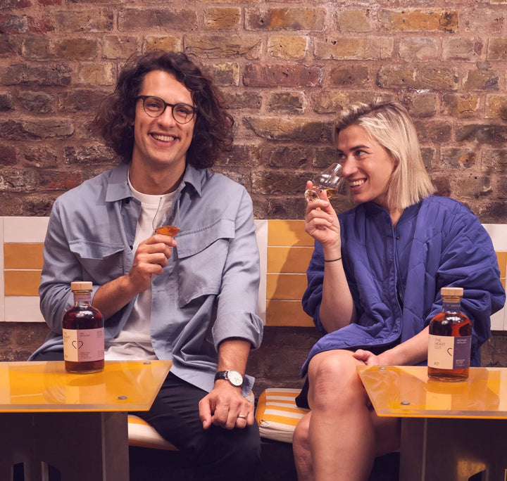 Fabrizio and Georgie from The Heart Cut sitting at a table with drinks against a brick wall.