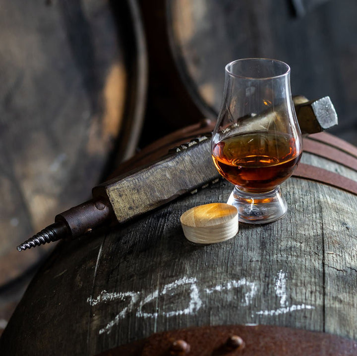 Glass of whisky on a wooden barrel with a barrel bung remover