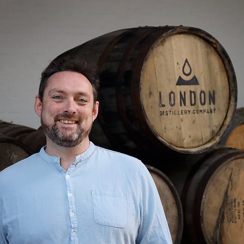 Matt McKay standing in front of wooden barrels with 'London Distillery Company' branding.