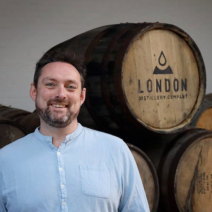 Matt McKay standing in front of wooden barrels with 'London Distillery Company' branding.