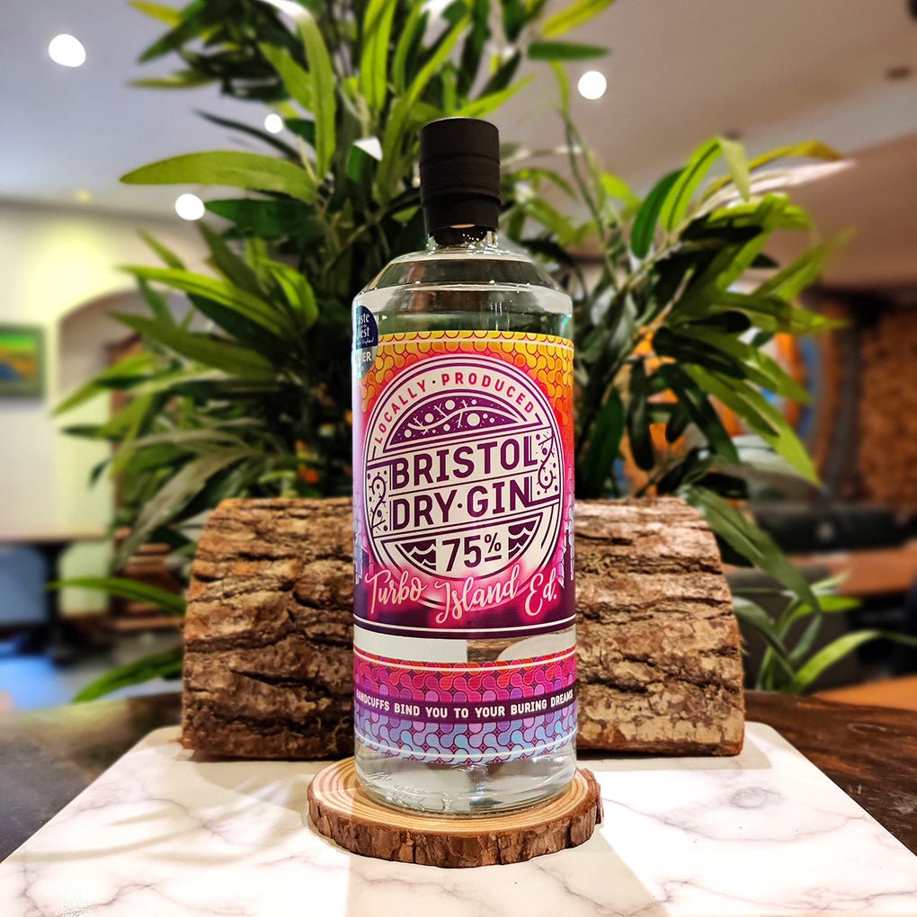 Bottle of Bristol Dry Gin Turbo Island Edition 75% alcohol on a wooden coaster with plants in the background