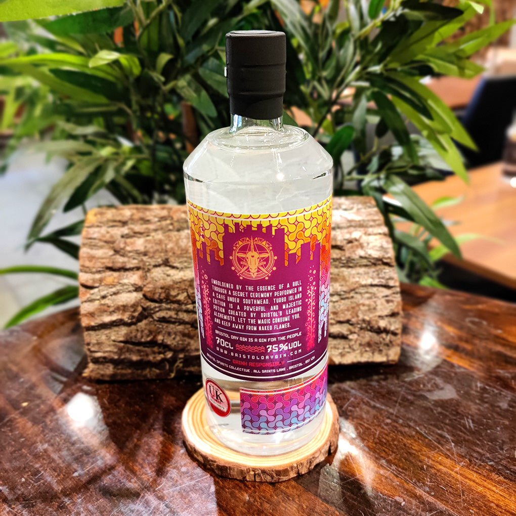 Bottle of Bristol Dry Gin Turbo Island Edition 75% alcohol back label on a wooden coaster, surrounded by greenery.