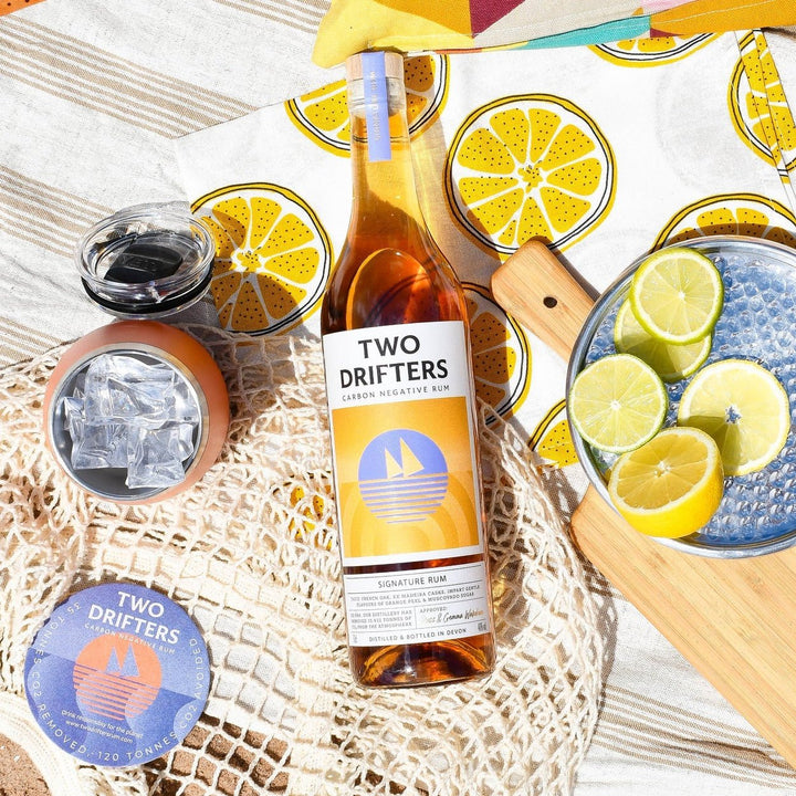 Bottle of 'Two Drifters' Signature rum on a beach setting with lemons and a colourful towel.