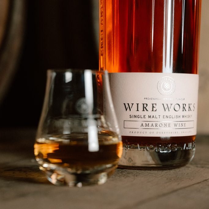 Bottle of Wire Works Amarone cask whisky with a glass of whisky on a wooden surface.