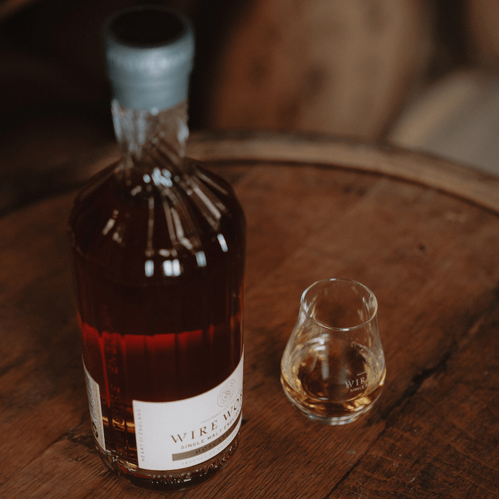 Bottle and glass of White Peak Distillery's Wire Works Amarone Cask English Whisky on a wooden barrel top