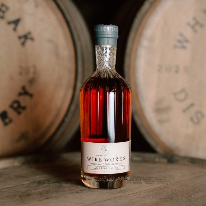 Bottle of Wire Works Amarone Cask whisky on wooden barrels with 'White Peak Distillery' branding.