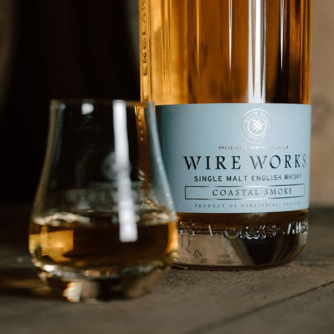 Wire Works Coastal Smoke single malt English whisky bottle with a glass on a wooden surface