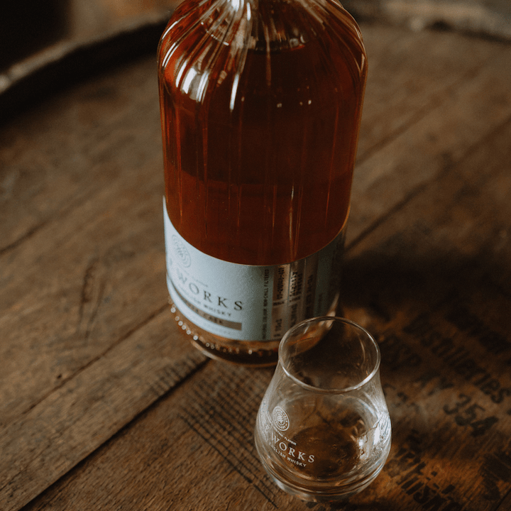 Bottle and glass of White Peak Distillery's Wire Works Coastal Smoke English Whisky on a wooden barrel top