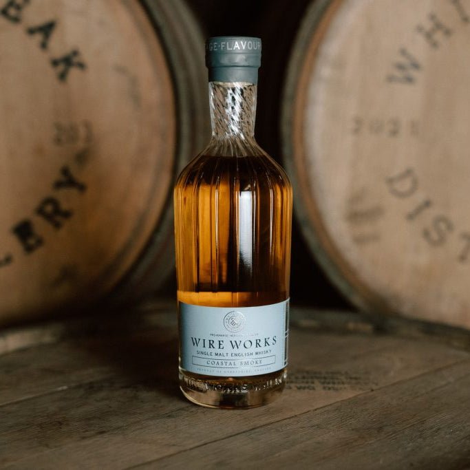 Bottle of Wire Works Coastal Smoke whisky in front of wooden barrels