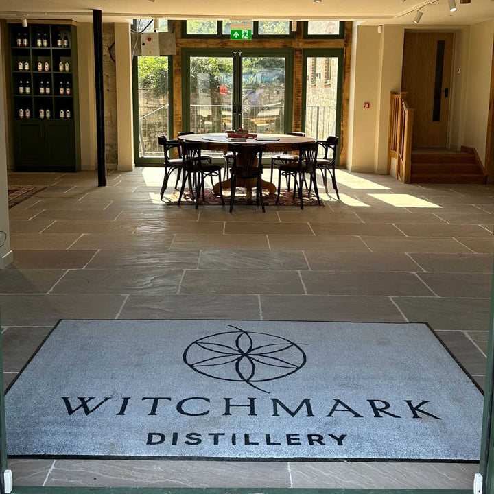 Witchmark Distillery Entrance Lobby area with a branded welcome mat and a table and chairs in the background
