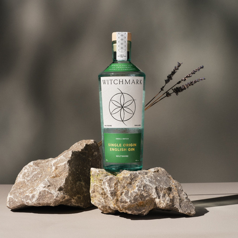 Bottle of Witchmark gin with a label featuring a witchmark logo, placed on a neutral background with rocks.